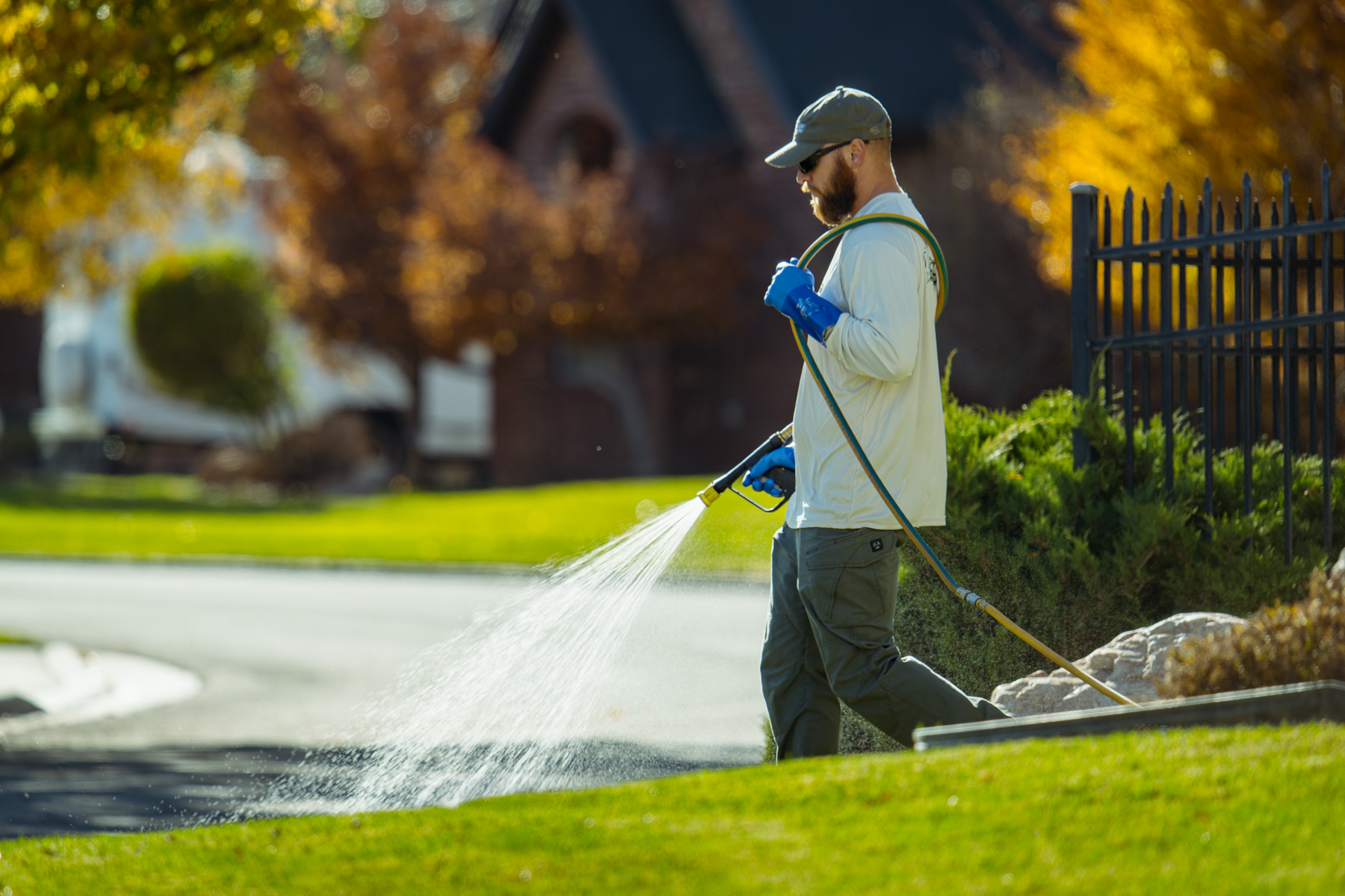 Technician applies weed control and fertilizer service with hose sprayer on residential lawn edge in Davis County Utah.